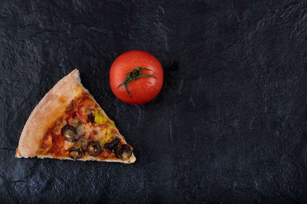 Morceau de délicieuse pizza à la tomate rouge fraîche placée sur un fond noir.