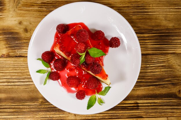 Morceau de délicieux cheesecake de New York avec des framboises et de la confiture de framboises dans une assiette blanche sur une table en bois. Vue de dessus
