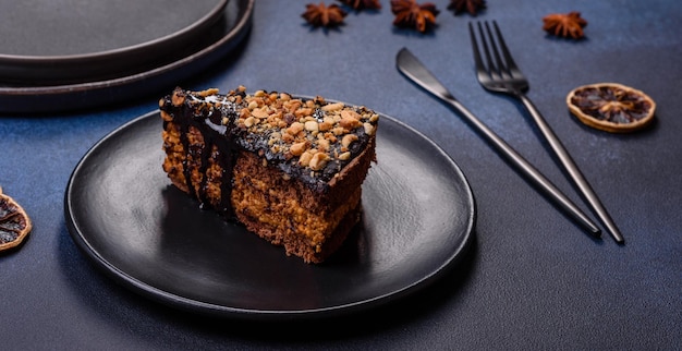 Un morceau de délicieux gâteau frais avec des noix et du chocolat sur une plaque noire sur un fond bleu foncé