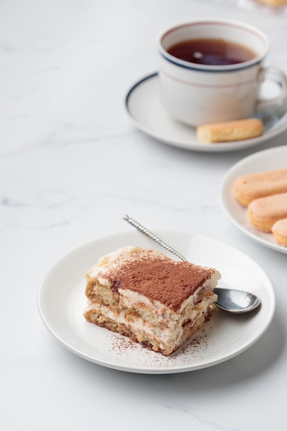 Morceau de dessert au gâteau tiramisu fait maison et café avec savoiardi comme ingrédients sur fond de marbre blanc