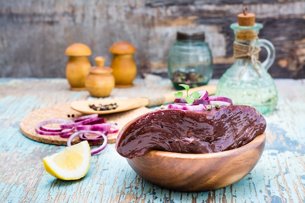 Un morceau de foie de boeuf cru dans un bol et des épices pour la cuisson sur une table en bois