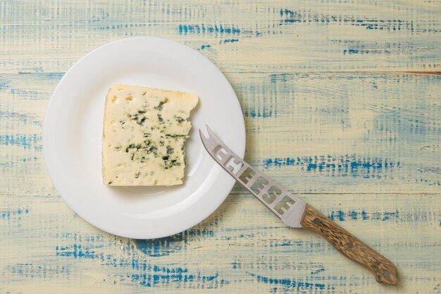 Un morceau de fromage bleu sur une assiette avec un couteau à fromage sur un fond de bois