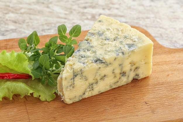 Morceau de fromage bleu à bord servi avec des feuilles de basilic