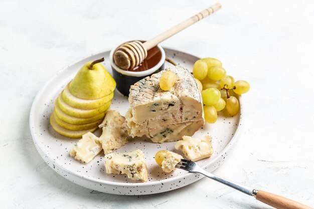 Morceau de fromage bleu, poire, raisins et miel sur fond clair Cuisine française Délicieuses collations au vin assorties pour le texte vue de dessus