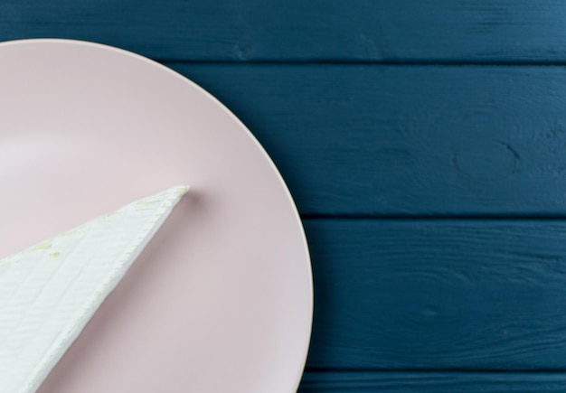 Un morceau de fromage brie sur une assiette sur un fond bleu foncé en bois