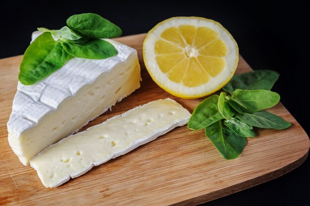 Un morceau de fromage Brie, de citron et d'épinards sont sur la planche à découper.