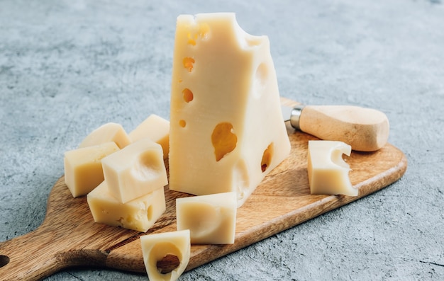 Morceau de fromage Maasdam au lait de vache sur une planche à découper en bois sur bsckground en béton.