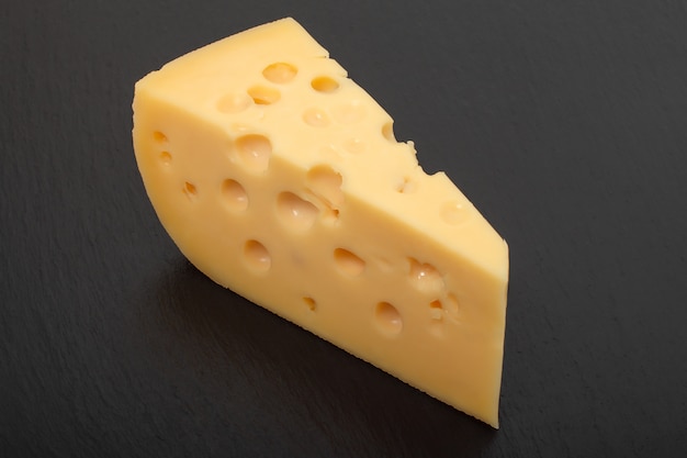 Morceau de fromage Maasdam jaune sur une planche de pierre noire