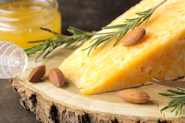 Un morceau de fromage marbré savoureux sur un support en bois avec des amandes, du romarin et du miel sur un fond sombre. fermer