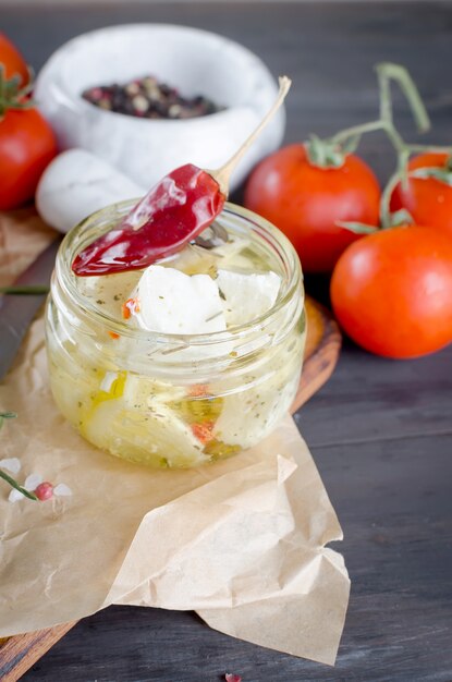 Morceau de fromage à pâte molle sur le plateau et féta épicée marinée dans un bocal et tomates pour la salade.