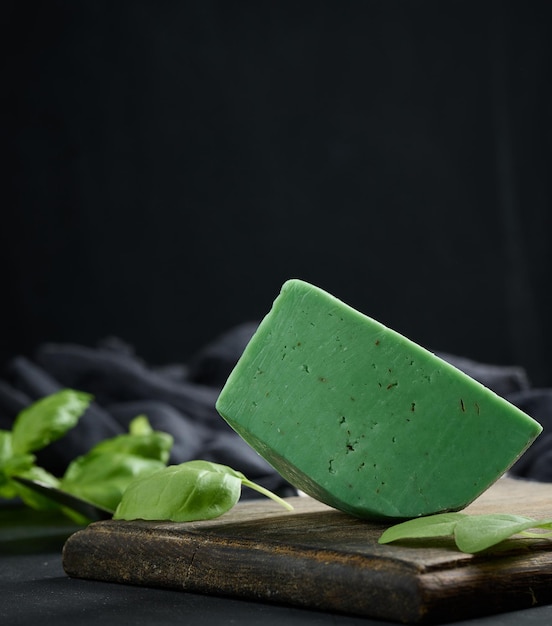 Un morceau de fromage vert au basilic sur une planche de bois marron fond noir