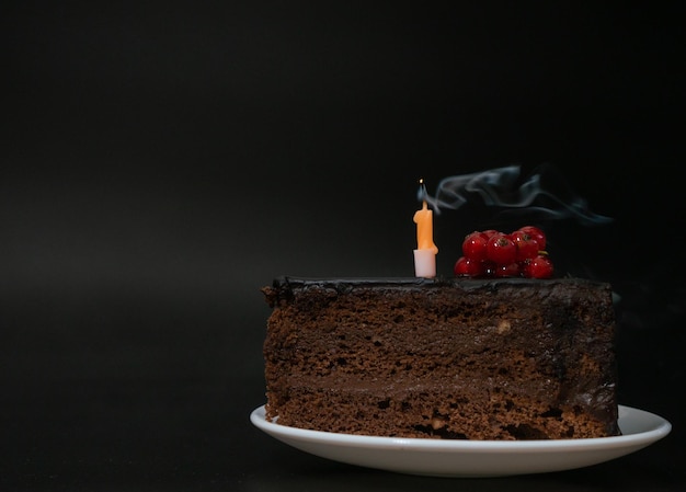 Morceau de gâteau d'anniversaire au chocolat avec une bougie éteinte sur plaque blanche sur fond noir profond