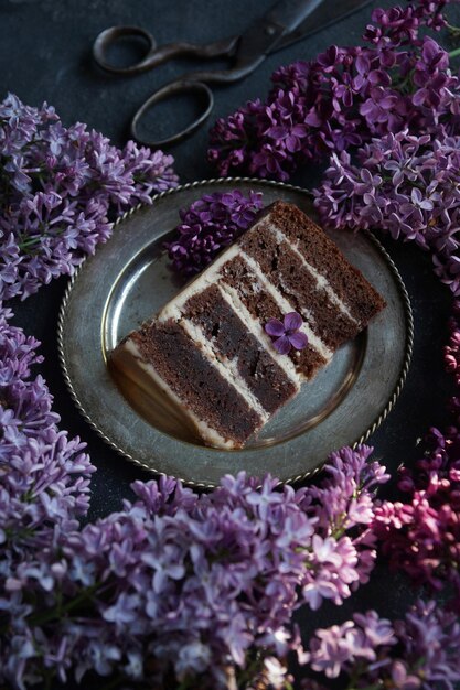 Morceau de gâteau au chocolat à la crème, tranché sur une assiette, avec lilas sur fond de pierre noire, mise au point sélective, gros plan