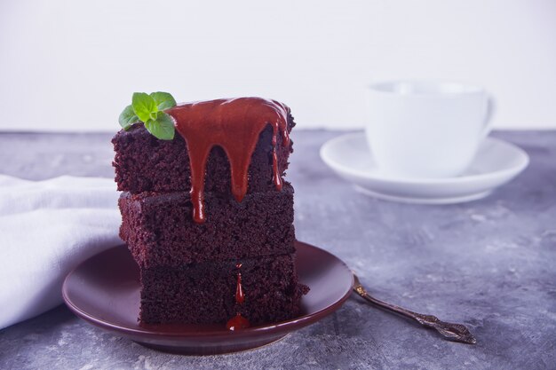 Un morceau de gâteau au chocolat fait maison sur la plaque avec du glaçage, une feuille de menthe et une tasse de thé