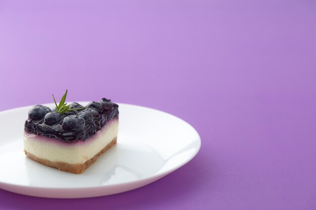 Morceau de gâteau au fromage aux bleuets sur plaque blanche sur fond violet