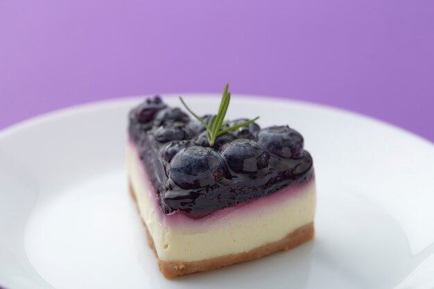 Morceau de gâteau au fromage aux bleuets sur plaque blanche sur fond violet