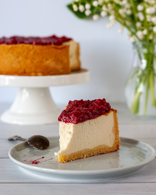 Un morceau de gâteau au fromage avec sauce aux framboises sur une assiette debout sur une table blanche.