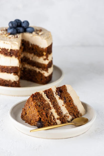 Morceau de gâteau aux carottes végétalien avec crème de noix de coco myrtilles noix et épices sur une assiette