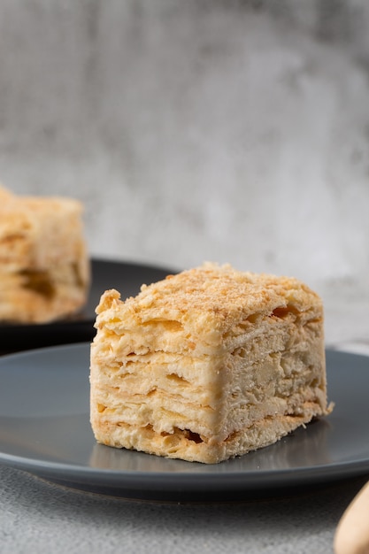 Morceau de gâteau Napoléon sur plaque bleue sur fond de marbre, vue rapprochée. Dessert millefeuille traditionnel avec pâte feuilletée et crème anglaise, copie espace. Photo verticale. Photo pour le menu boulangerie.