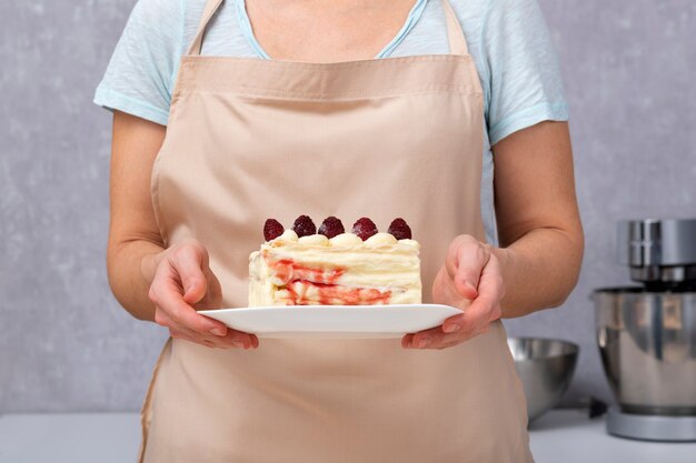 Morceau de gâteau de tranche de vanille avec des baies dans les mains du cuisinier.