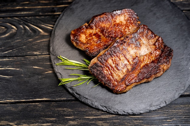 Morceau juteux de viande frite se trouve sur une plaque de pierre contre une table en bois noire