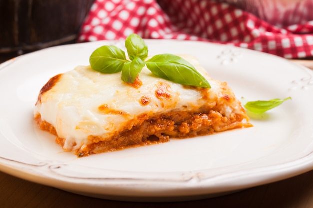 Morceau de lasagne bolognaise aux feuilles de basilic dans une assiette blanche