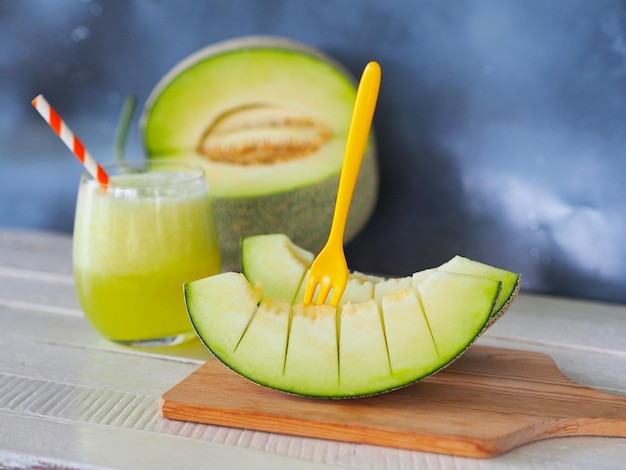 Morceau de melon vert ou de miellat sur une planche à découper en bois et un verre de jus de melon