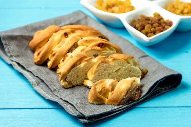 Morceau de pain tressé sucré avec des raisins secs sur un torchon sur un fond en bois bleu.