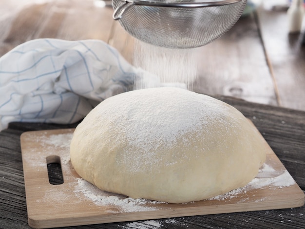 Photo morceau de pâte ronde pour pizza sur une planche à découper en bois