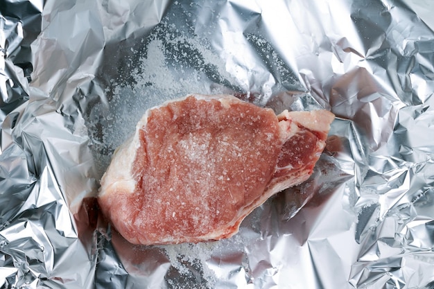 Un morceau de porc en grains de sel se trouve sur le papier d'aluminium prêt pour la cuisson vue de dessus
