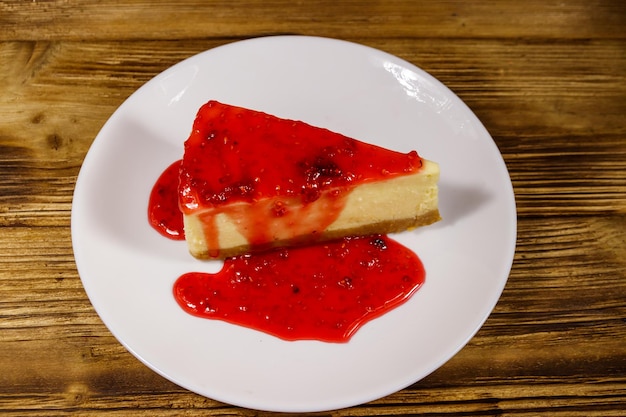 Morceau de savoureux cheesecake de New York avec confiture de framboises dans une assiette blanche sur table en bois