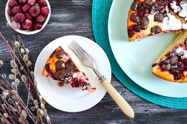 Morceau de tarte au fromage cottage avec des cerises et des gouttes de chocolat sur une plaque sur une surface en bois. La vue de dessus