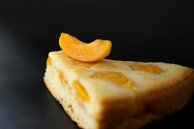 Morceau de tarte aux abricots humide avec une tranche de fruit d'abricot sur fond sombre