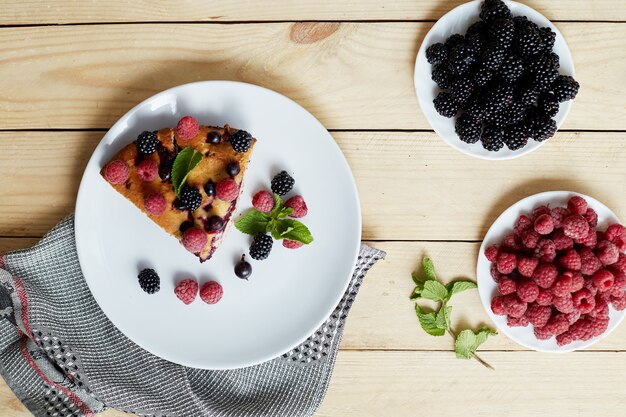 Morceau de tarte aux myrtilles, framboises et menthe pour le dessert sur une assiette blanche, serviette. Morceaux de délicieux gâteau fait maison sur une table en bois