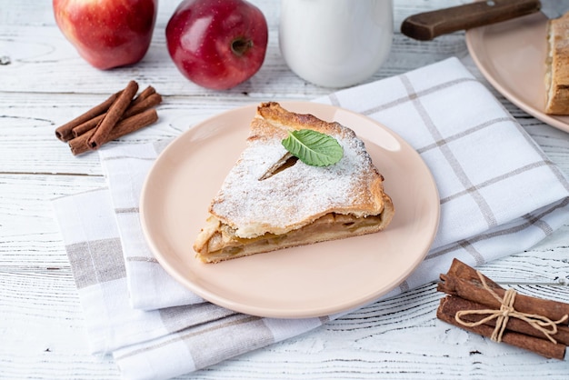 Morceau de tarte aux pommes fait maison avec des pommes rouges fraîches sur tableau blanc