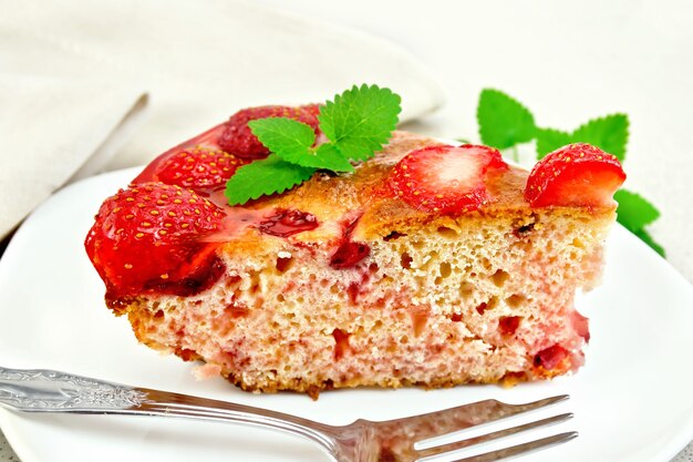 Morceau de tarte sucrée aux fraises, kissel, gelée et menthe, fourchette en plaque blanche sur fond planche de bois
