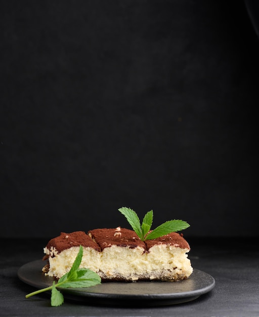 Un morceau de tiramisu saupoudré de cacao sur un brin de menthe fraîche sur fond noir