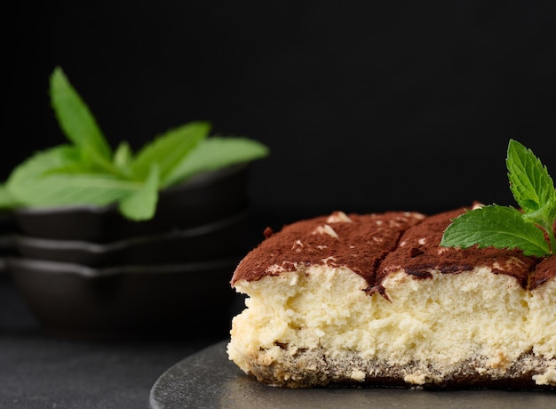 Un morceau de tiramisu saupoudré de cacao sur un brin de menthe fraîche sur fond noir