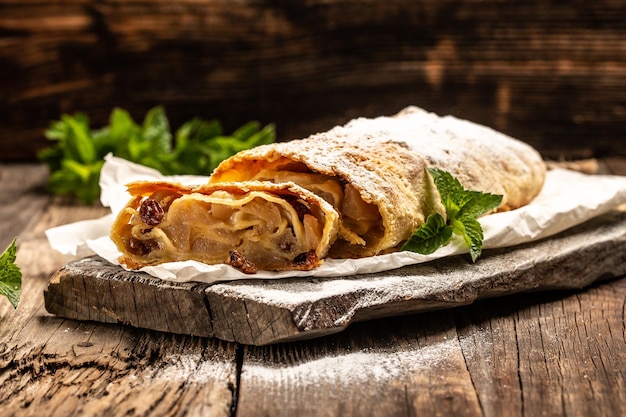 Morceau traditionnel de strudel aux pommes avec sucre en poudre et gros plan de menthe sur un espace de copie de fond en bois