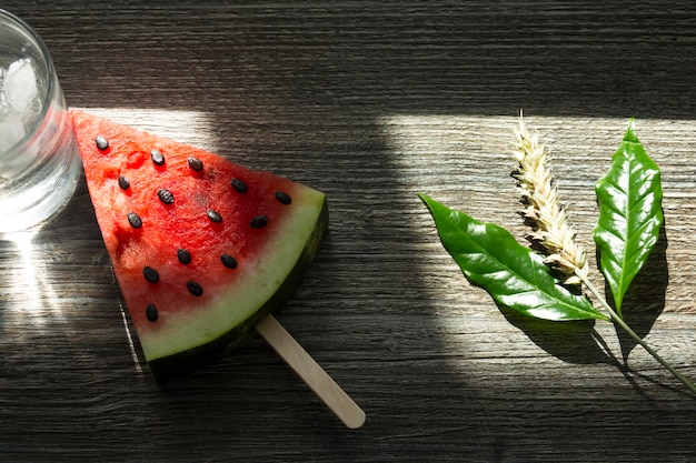 Un morceau triangulaire de pastèque sucrée sur une étagère de crème glacée une boisson froide avec de la glace et des épis de blé mûrs sur une surface en bois