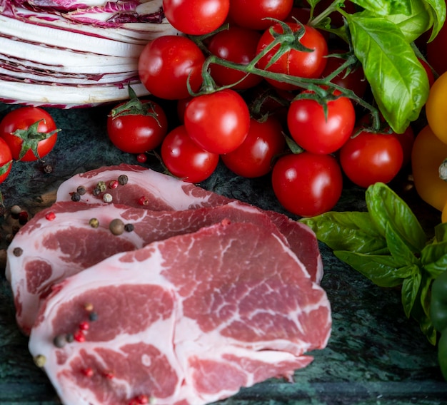 Morceau de viande frais, épices et légumes assortis sur planche de marbre vert foncé