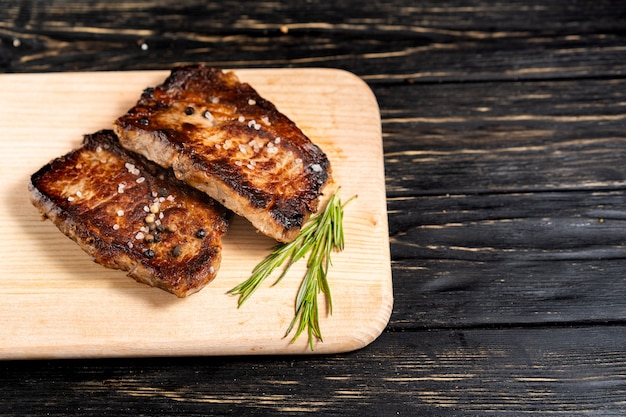 Un morceau de viande frite juteuse se trouve sur une planche à découper contre une table en bois noire