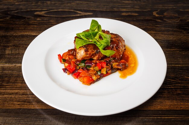 Morceau de viande juteux avec légumes cuits et sauce au basilic et à la crème sur une assiette blanche.