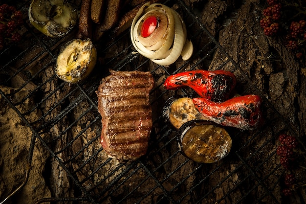 Un morceau de viande rôtie avec des légumes sur le gril sur un fond d'écorce d'arbre