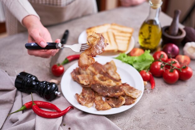 Morceaux de bacon frits dans une assiette et légumes sur une table en pierre ou en béton de cuisine domestique