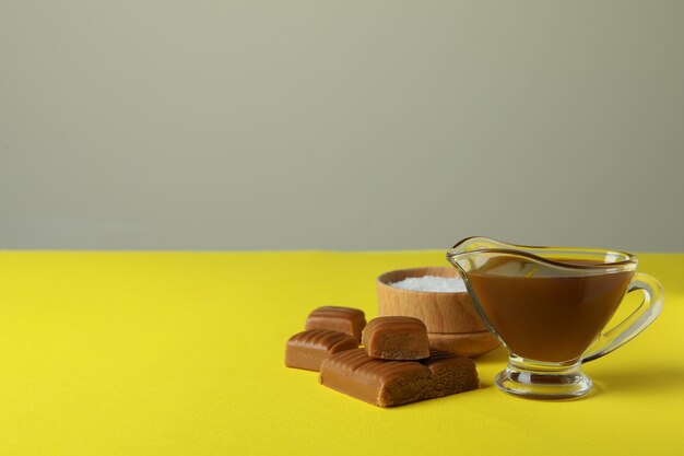 Morceaux de caramel, sauce et bol de sel sur table jaune