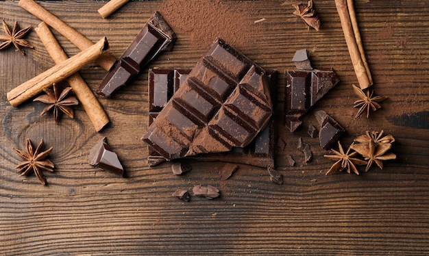 Morceaux cassés de chocolat noir, bâtons de cannelle et anis étoilé sur une table en bois marron, vue de dessus