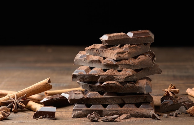 Morceaux cassés de chocolat noir, de bâtons de cannelle et d'anis étoilé sur une table en bois marron