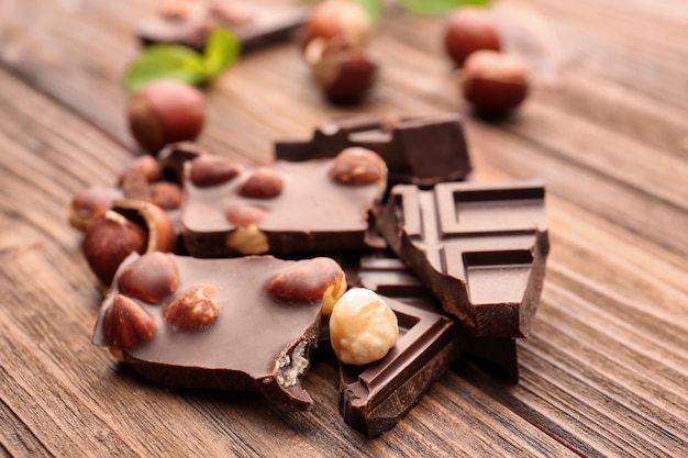 Morceaux de chocolat cassés avec des noix et des feuilles de menthe sur table en bois