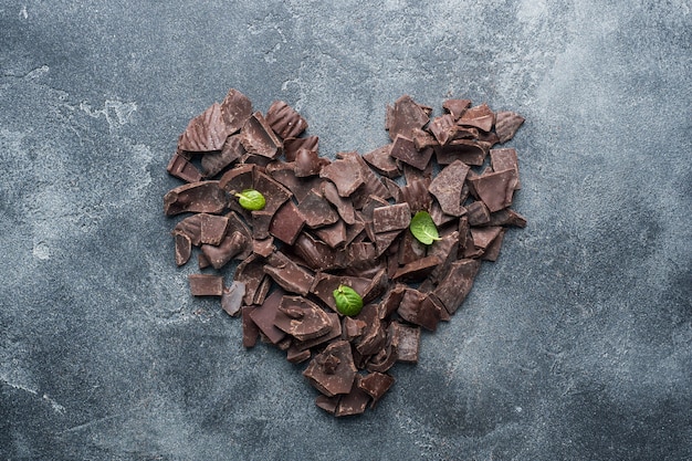 Morceaux de chocolat noir broyé avec des feuilles de menthe en forme de cœur sur un fond texturé foncé.